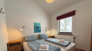 Une chambre avec deux lits, une table de chevet, une lampe, un tableau et une fenêtre donnant sur un beau paysage.