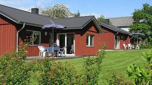 Un bâtiment rouge doté d’un patio couvert, d’un espace extérieur aménagé avec des sièges et d’une pelouse.
