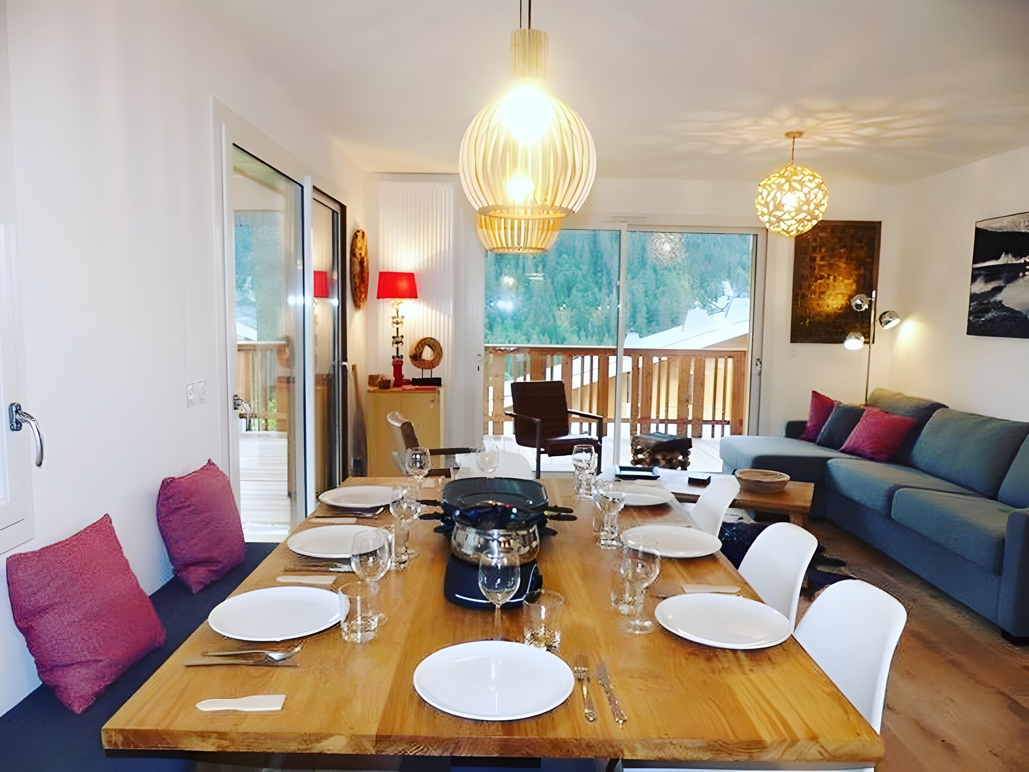 A dining area with a wooden table set for four, a sofa, and a view of a snowy landscape.