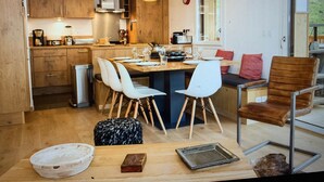 A modern kitchen with wooden cabinets, a dining area with white chairs, and pendant lighting. - Apartment "Les Loges Blanches 101" with Wi-Fi (Châtel)