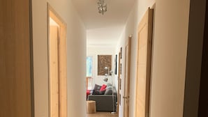 A hallway with wooden flooring, a ceiling fan, and a bed with pillows in the background. - Apartment "Les Loges Blanches 101" with Wi-Fi (Châtel)