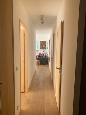 A hallway with wooden flooring, a ceiling fan, and a bed with pillows in the background.