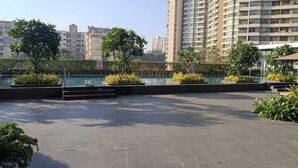 A rooftop terrace with a swimming pool, surrounded by greenery and tall buildings in the background. - 
Luxury Apartment at Oberoi Maxima Near Airport Andheri Mumbai (Mumbai)