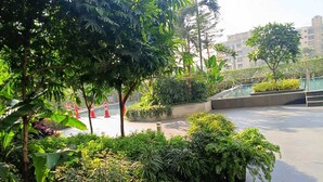 A rooftop garden with various plants and trees, a paved walkway, and a view of buildings in the background. - 
Luxury Apartment at Oberoi Maxima Near Airport Andheri Mumbai (Mumbai)
