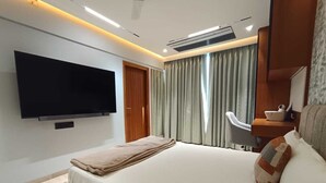 A modern hotel room with a large bed, a flat-screen TV mounted on the wall, a desk with a chair, and a window with curtains. - 
Luxury Apartment at Oberoi Maxima Near Airport Andheri Mumbai (Mumbai)