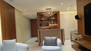 A modern living room with a round grey armchair, a white sofa, a wooden reception desk with a chandelier, and a flat-screen TV mounted on the wall. - 
Luxury Apartment at Oberoi Maxima Near Airport Andheri Mumbai (Mumbai)