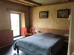 Ein Schlafzimmer mit einem Bett, einem Sessel, einem Fenster und zwei gerahmten Bildern an der Wand.
