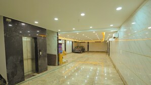 Um corredor amplo com piso de mármore, um elevador e um carro estacionado.