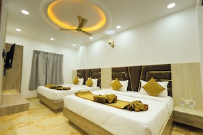 A hotel room with two beds, a ceiling fan, recessed lighting, a TV mounted on the wall, and a small table with toiletries. - Maa Kela Devi Shanti Atithi Bhawan (Vrindavan)