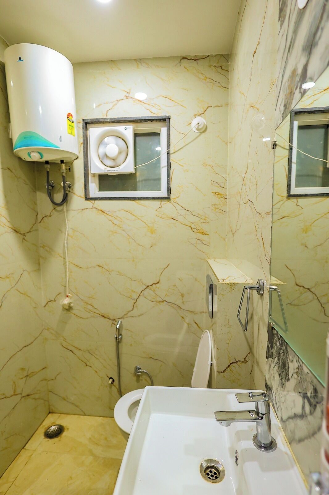 Ein Badezimmer mit Marmorwand, Waschbecken in Weiß, Toilette, Duschbrause und Wandheizung.