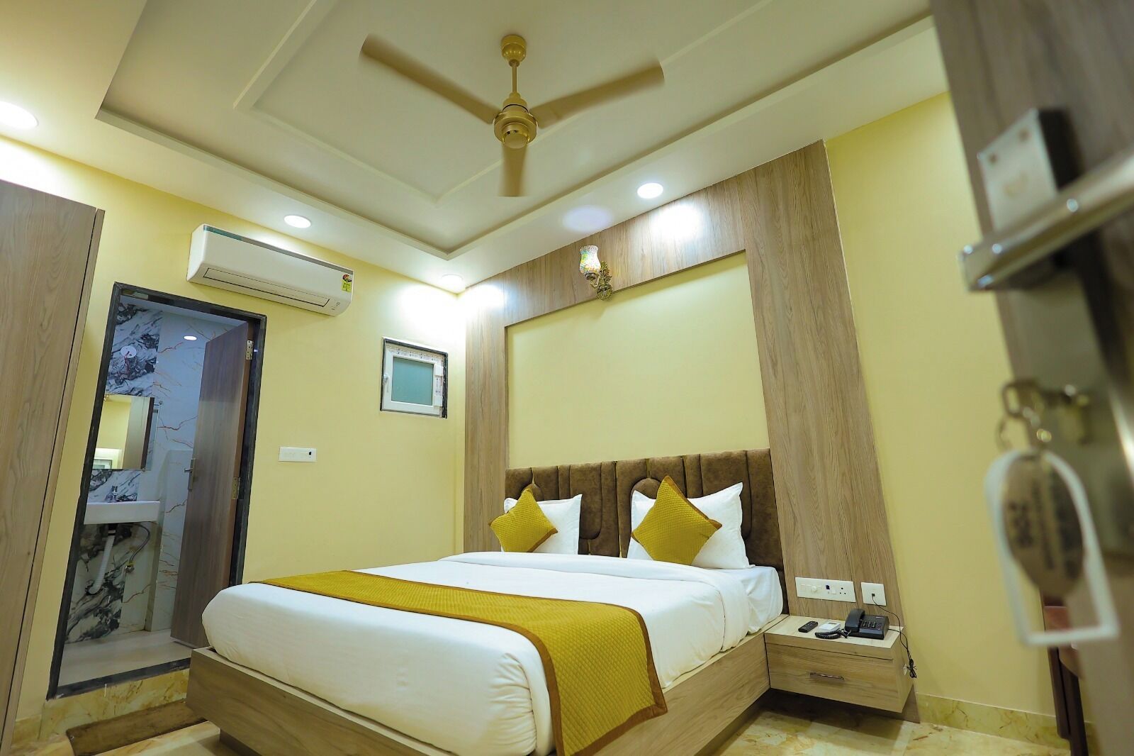 Une chambre d’hôtel comprenant un lit, des tables de chevet, un appareil de climatisation, un ventilateur de plafond et une petite lampe de chevet.
