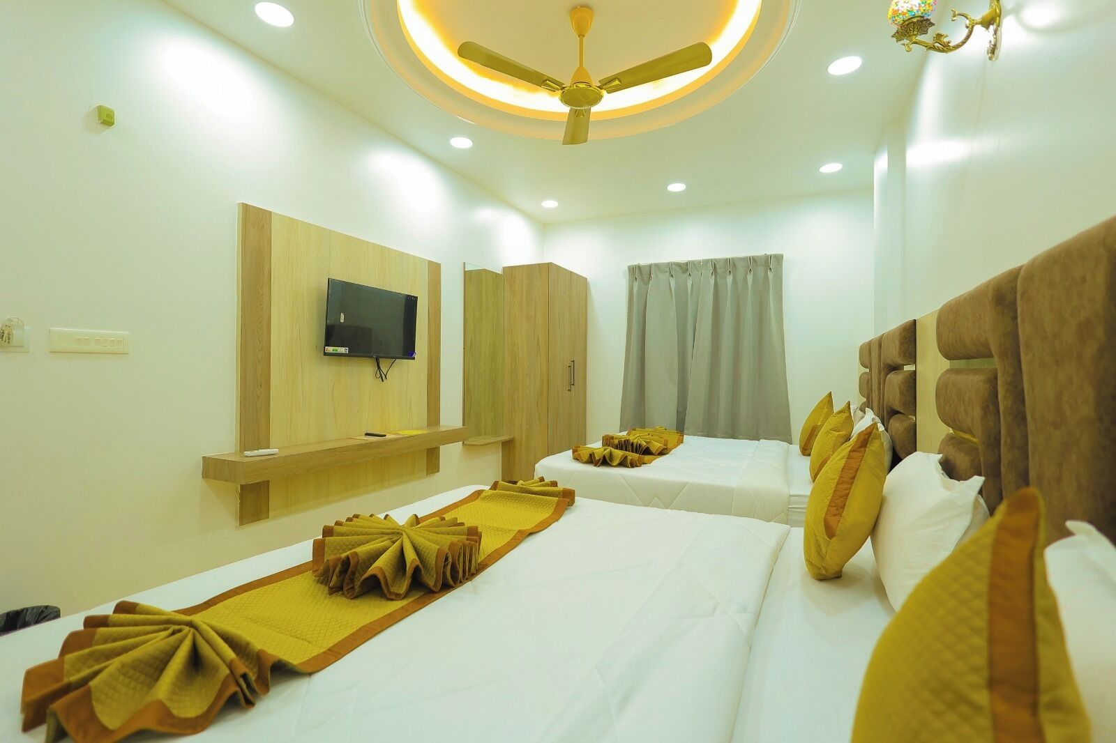 Une chambre d’hôtel avec deux lits, un ventilateur de plafond, une télévision et une fenêtre avec des rideaux.
