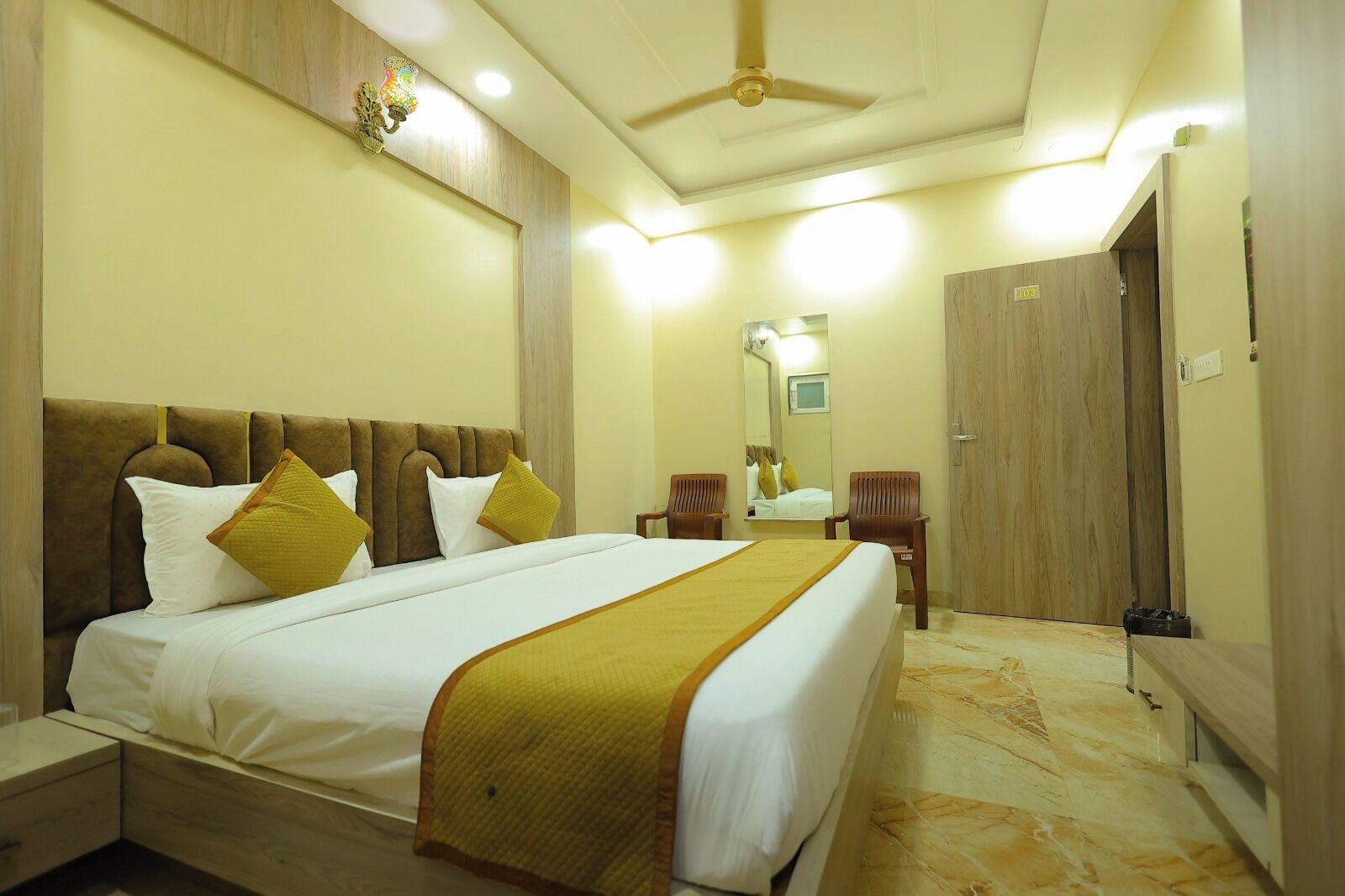 Habitación de hotel con una cama grande, cabecera de madera, espejo, armario y ventilador de techo.