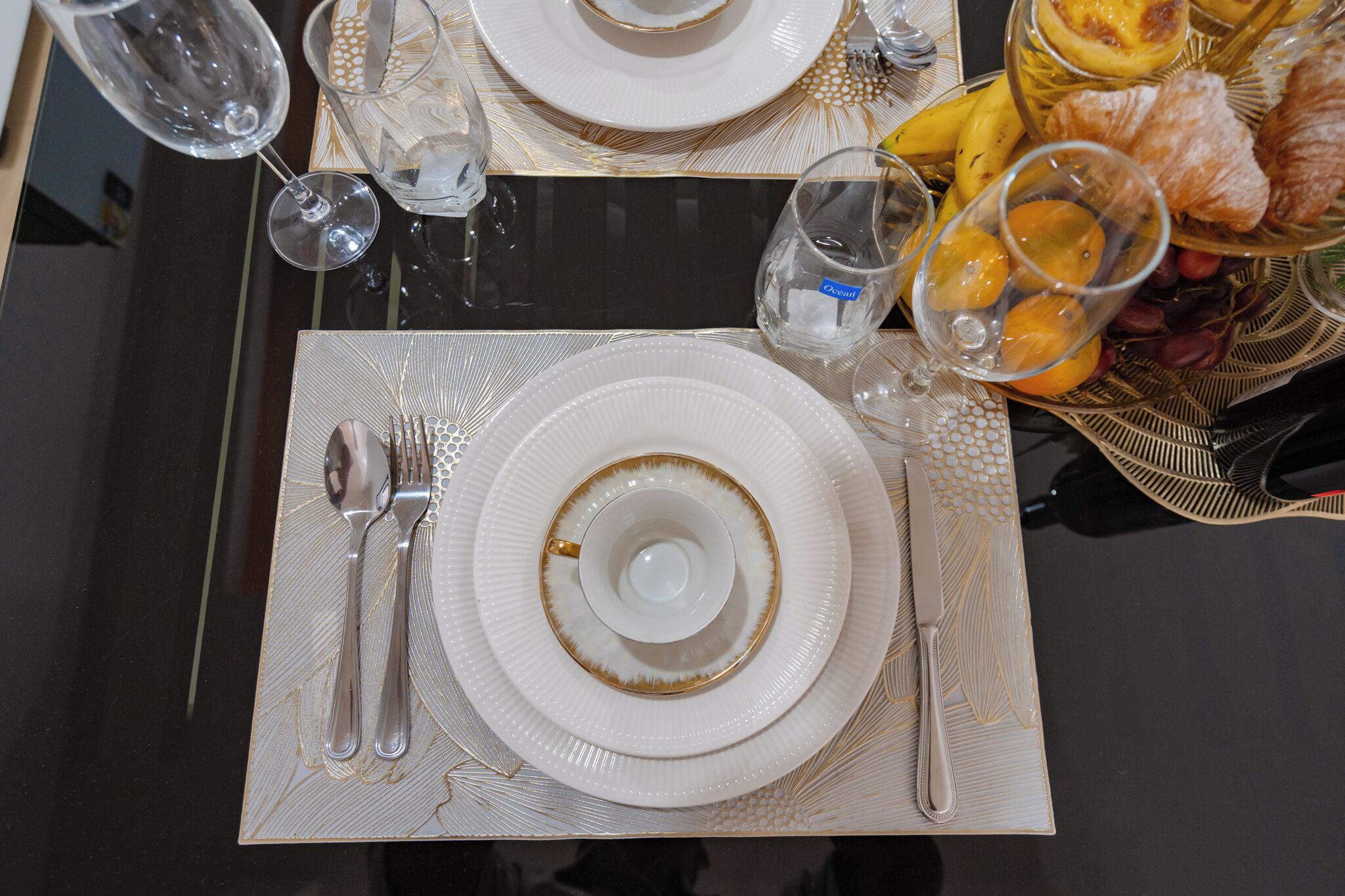 A dining table set with white plates, silverware, and clear glasses.