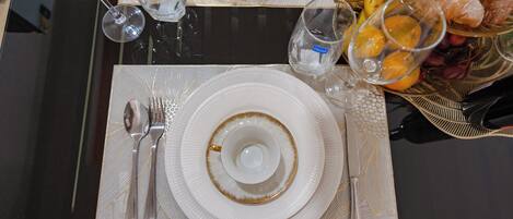 A dining table set with white plates, silverware, and clear glasses.