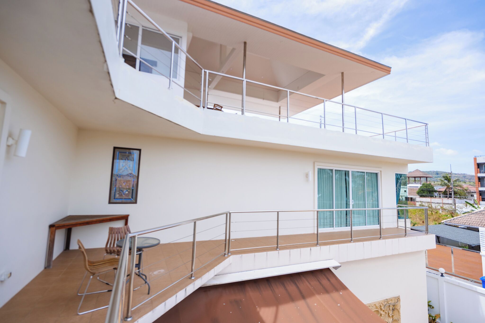 Ein modernes, zweistöckiges Gebäude mit Balkon, einem Essbereich mit Stühlen und Tisch sowie Blick auf die umliegende Nachbarschaft.