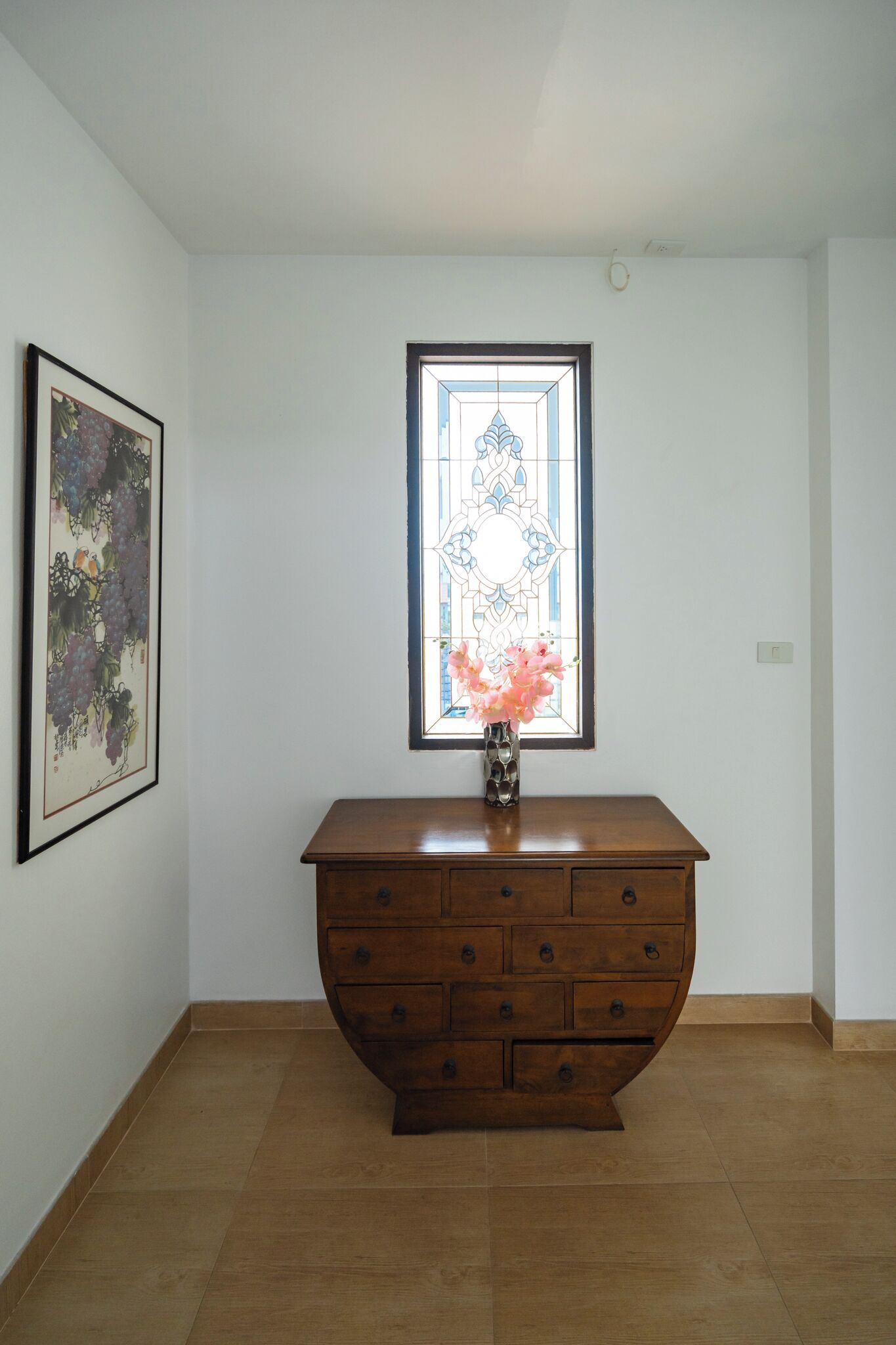 Ein Zimmer mit einem Holzkasten, einem gerahmten Kunstwerk und einem Fenster mit Buntglasdekor.