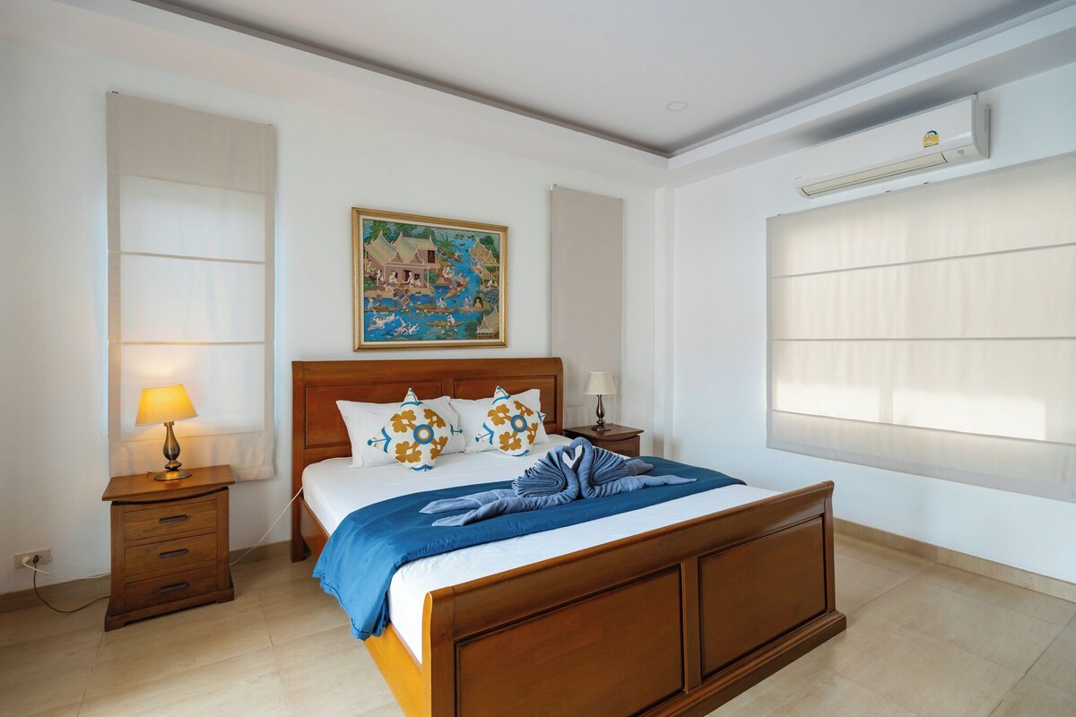 Ein Hotelzimmer mit einem hölzernen Bett, einem Nachttisch mit Lampe, einem Gemälde an der Wand und einer Klimaanlage.