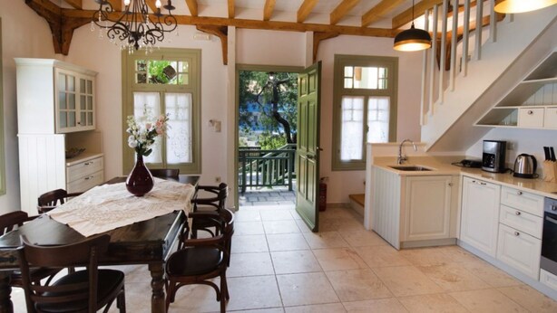 Una cocina amplia con vigas de madera, un comedor con una mesa dispuesta para cuatro personas y vistas al balcón exterior.