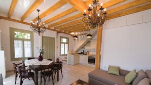 Amplia sala de estar con una mesa de comedor, sillas de madera, un sofá y una escalera que lleva a una cocina.