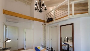 Habitación de hotel con dos camas, una araña, un espejo grande y una zona de descanso superior tipo loft.
