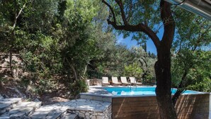 Una escalera de piedra conduce a una terraza de madera con piscina, rodeada de árboles.