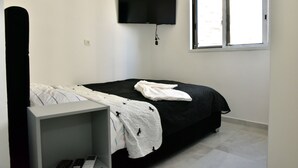 A bedroom with a bed, a TV mounted on the wall, a window, and a bedside table. - 2-bedroom Luxury apartment On The Sea Bat Yam (Bat Yam)