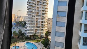 A high-rise building with a pool area visible through a window. - 2-bedroom Luxury apartment On The Sea Bat Yam (Bat Yam)