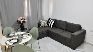 A modern living room with a grey sectional sofa, a dining table with green chairs, and a vase of flowers. - 2-bedroom Luxury apartment On The Sea Bat Yam (Bat Yam)