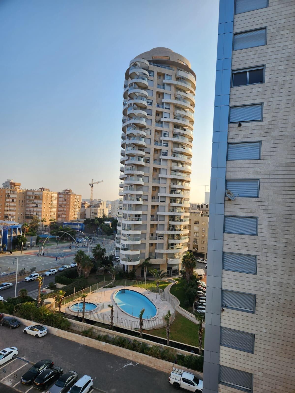 A high-rise residential building with a circular pool surrounded by greenery.