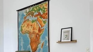 Una habitación con un sillón verde, una mesita de madera, un cuadro enmarcado y un mapa mundial en la pared.