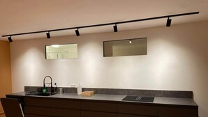 Uma cozinha moderna com bancada escura, pia e forno embutido. Há dois espelhos fixados na parede acima da bancada.