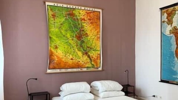 A bedroom with a bed, a chair, and two large wall maps. - Copy of Emma's Hostel (Duisburg)