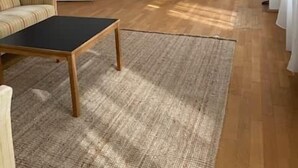 A modern living room with a sofa, a coffee table, and a rug. There is a dining area with a table and chairs, and a kitchen with cabinets and appliances. - Copy of Emma's Hostel (Duisburg)