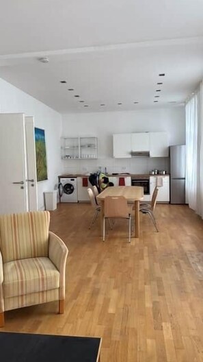 A modern kitchen with white cabinets, a dining table with chairs, and a striped armchair.