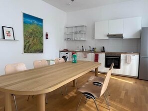 A modern kitchen with white cabinets, a wooden dining table, and a single chair.
