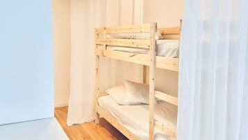 Dormitorio con literas, suelo de madera, paredes blancas y una lámpara colgante.