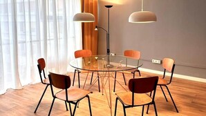 A modern dining area with a round glass table surrounded by six chairs, a tall floor lamp, and sheer curtains on the windows. - Emmas Lofts - City center location (Essen)
