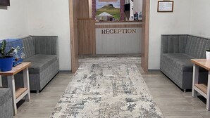 Ein Empfangsbereich mit einer Rezeption, zwei grauen Sofas, einem gemusterten Teppich und Uhren, die verschiedene Zeitzonen anzeigen.
