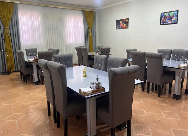 A conference room with six tables and chairs, a chandelier, and a painting on the wall. - Danexan Apa Hostel (Nukus)