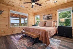 Un dormitorio de cabaña de madera con cama, banco, mesita de noche y ventilador de techo.
