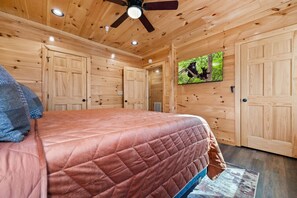 A wooden cabin bedroom with a bed, a ceiling fan, and a television screen displaying a bear. - Majestic Horizon by Ghosal Luxury Lodging (Sevierville)