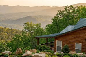 A cabin with a metal roof, surrounded by a rocky landscape and dense forest, overlooking a range of mountains. - Majestic Horizon by Ghosal Luxury Lodging (Sevierville)