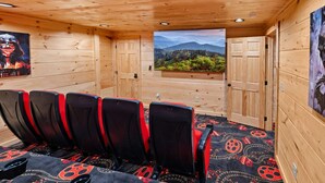 Una baita in legno con un angolo salotto caratterizzato da sedie rosse e nere, un tappeto decorato e vista su un bosco attraverso una porta.