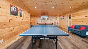 Un tavolo da ping pong con rete in una stanza con pareti in legno e un divano con cuscini rossi.