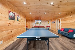 Ein Tischtennistisch mit Netz in einem Raum mit Holzwänden und einer roten Sofaecke.