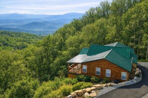 A cabin with a green roof, surrounded by dense forest and mountains in the background. - Majestic Horizon by Ghosal Luxury Lodging (Sevierville)