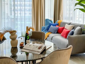 Un salon moderne avec une table en verre, un canapé agrémenté de coussins colorés et une bouteille de champagne.