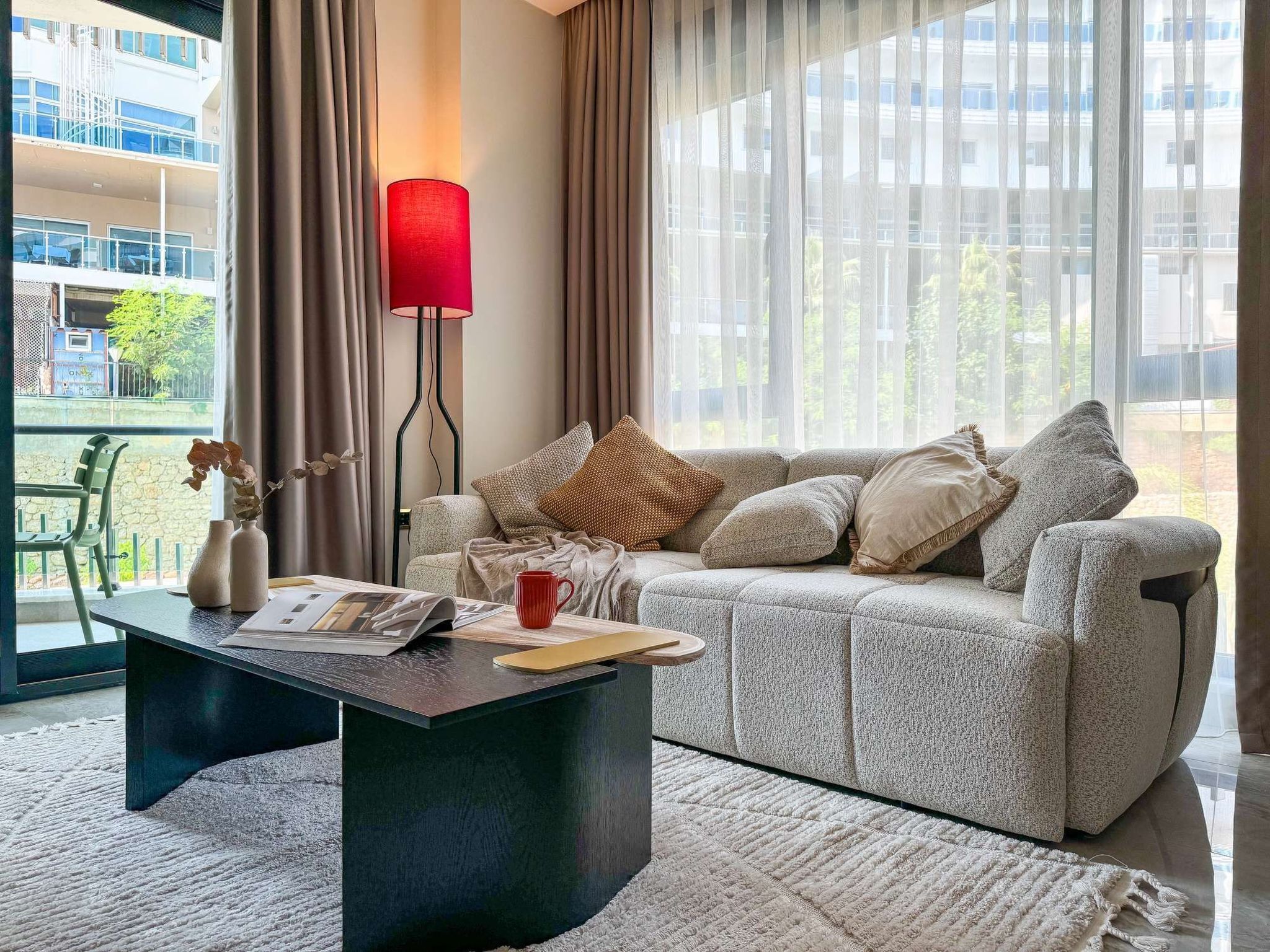 Ein modernes Wohnzimmer mit einem grauen Sofa, einem schwarzen Couchtisch und einer roten Stehlampe.