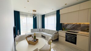 Een moderne woonkamer met een bank, een eettafel met stoelen, en een keuken met een fornuis en kastjes.